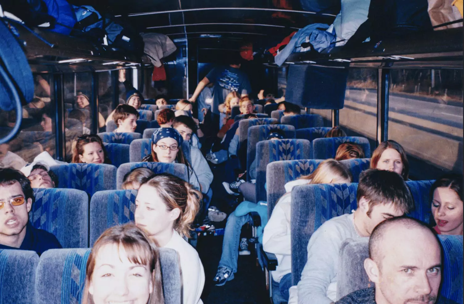 Film photo circa 2001, with people sitting in two rows of double seats on a big bus, transporting them to Northern Wisconsin.